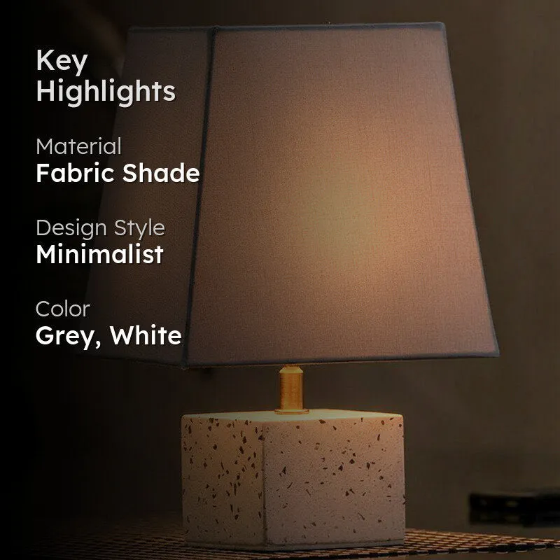 Lit grey fabric table lamp with white speckled base in a dark setting