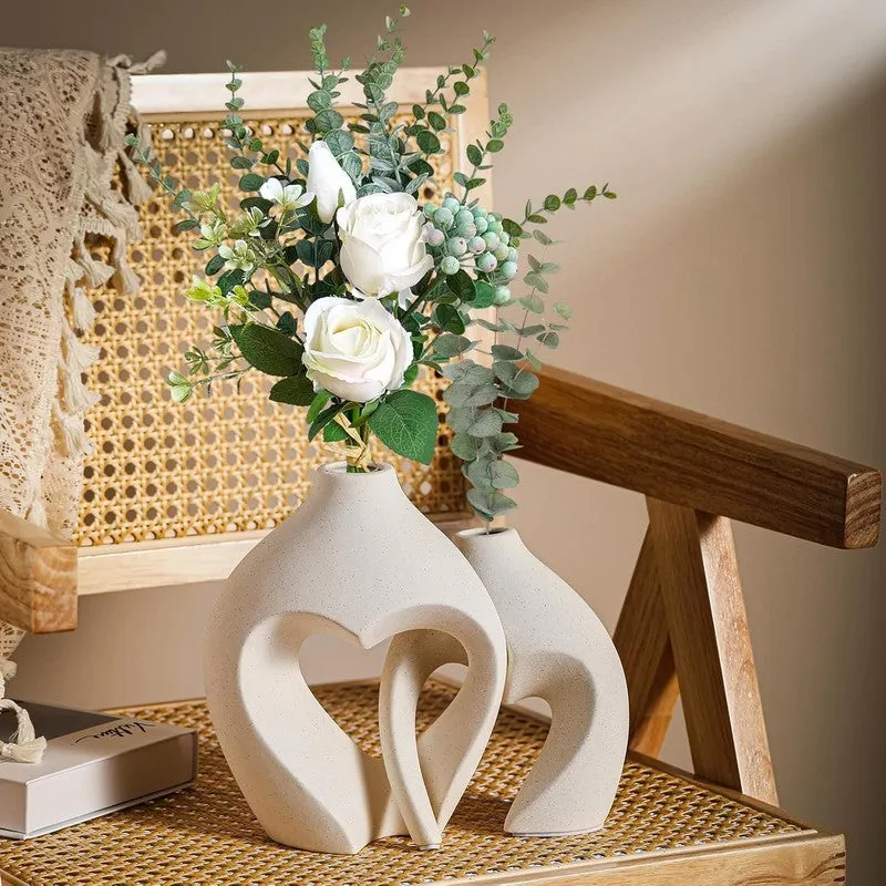 Two white sculptural vases with floral stems on a woven chair seat