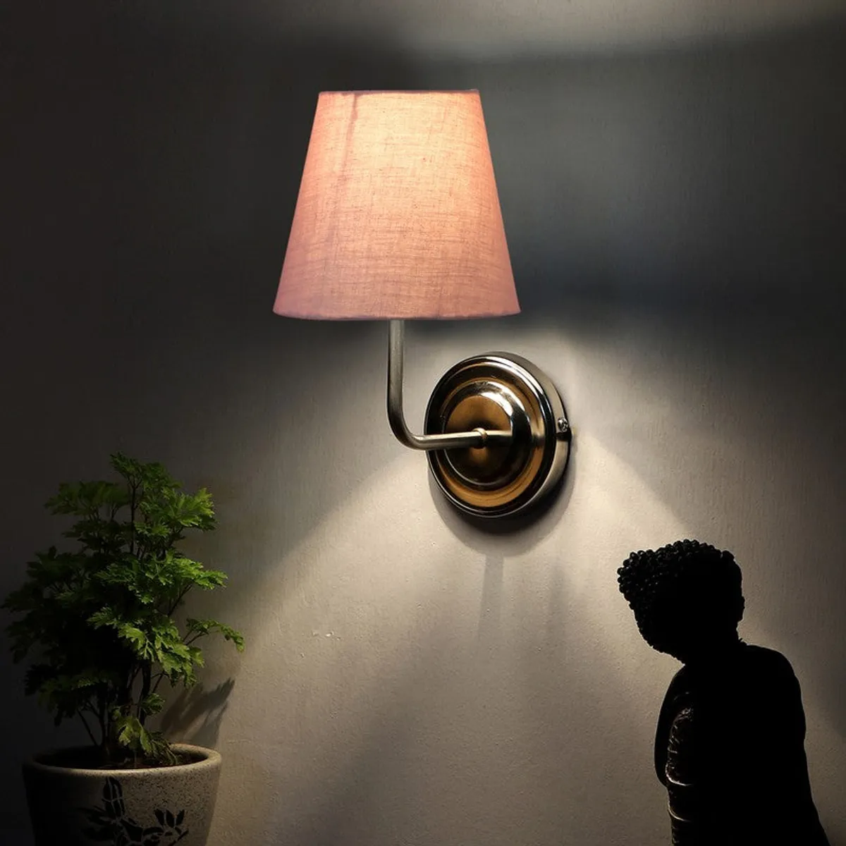 Dusty pink wall lamp casting upward light on a wall