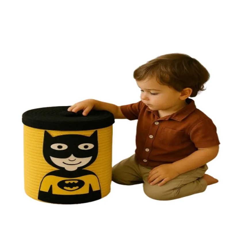 Child beside a yellow superhero-themed storage basket with black lid