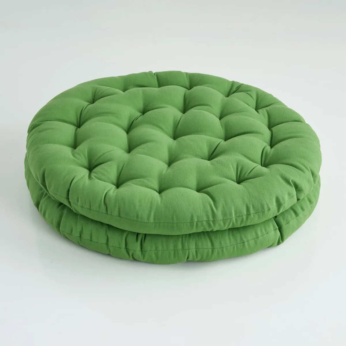 Stacked round light green floor cushions on a plain background