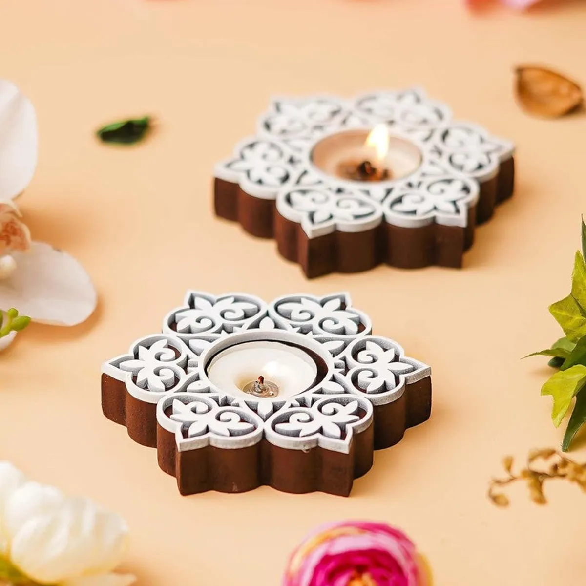 Two floral wooden tea light holders with tea lights on a beige setting