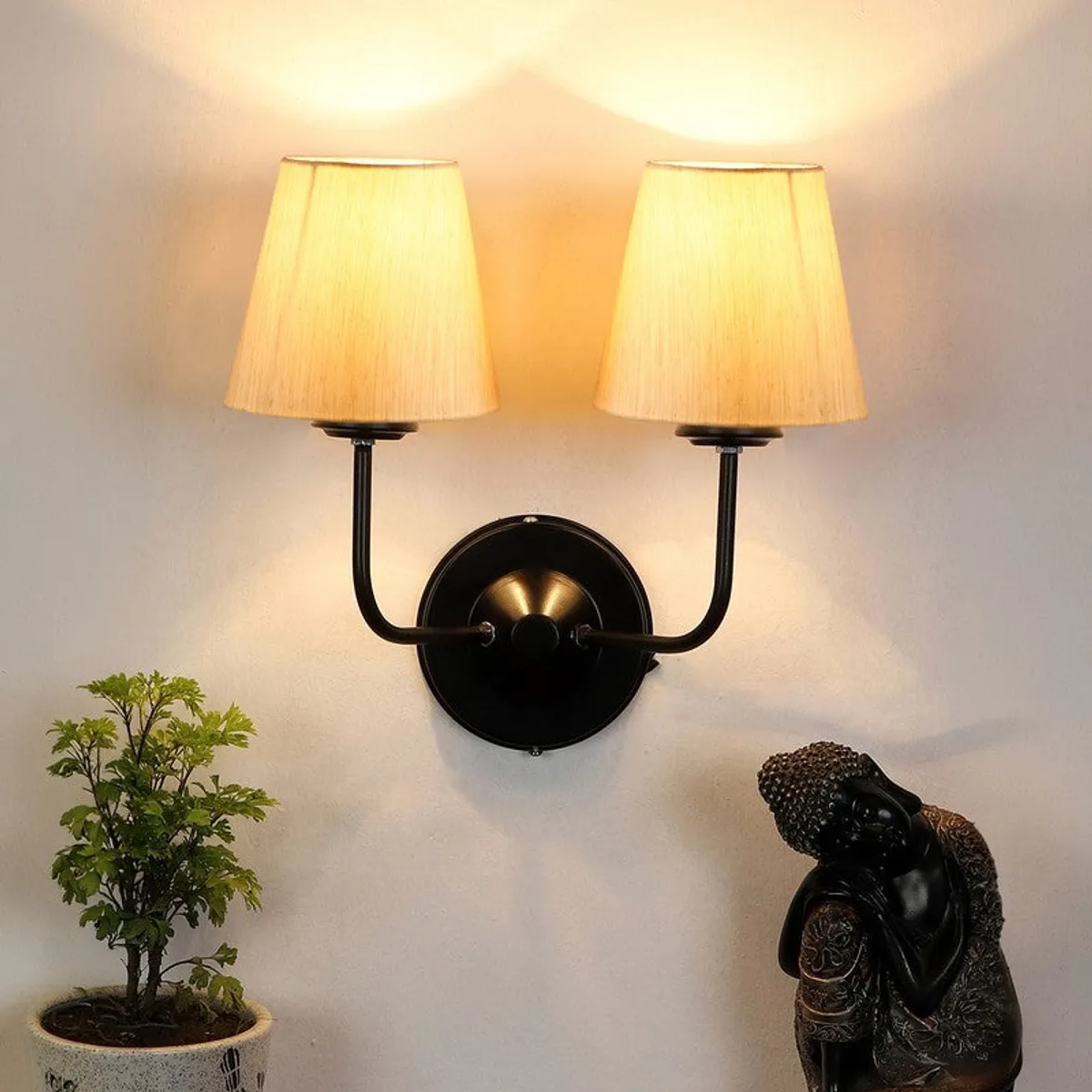 Twin beige shade wall lamp glowing warmly above a black round base