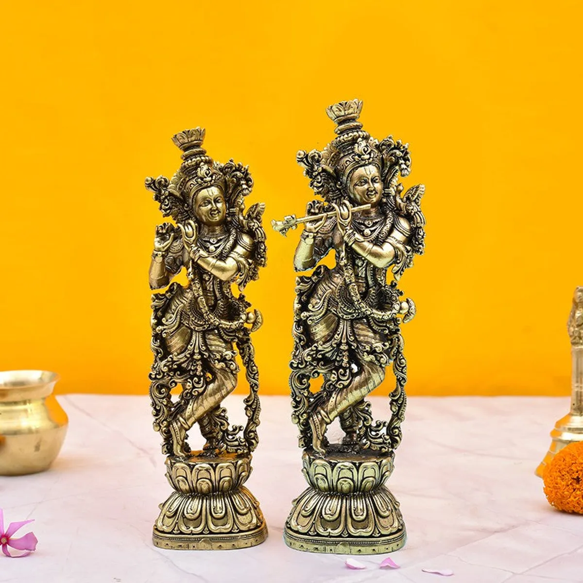 Pair of ornate gold-toned Venugopala idols against a bright yellow backdrop