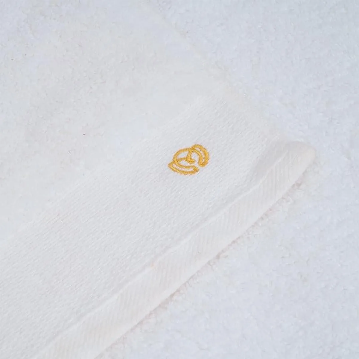 Close-up of the white towel showing its plush texture and gold embroidered accent
