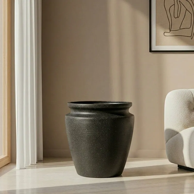 Black floor planter with a wide rim beside a light-coloured armchair