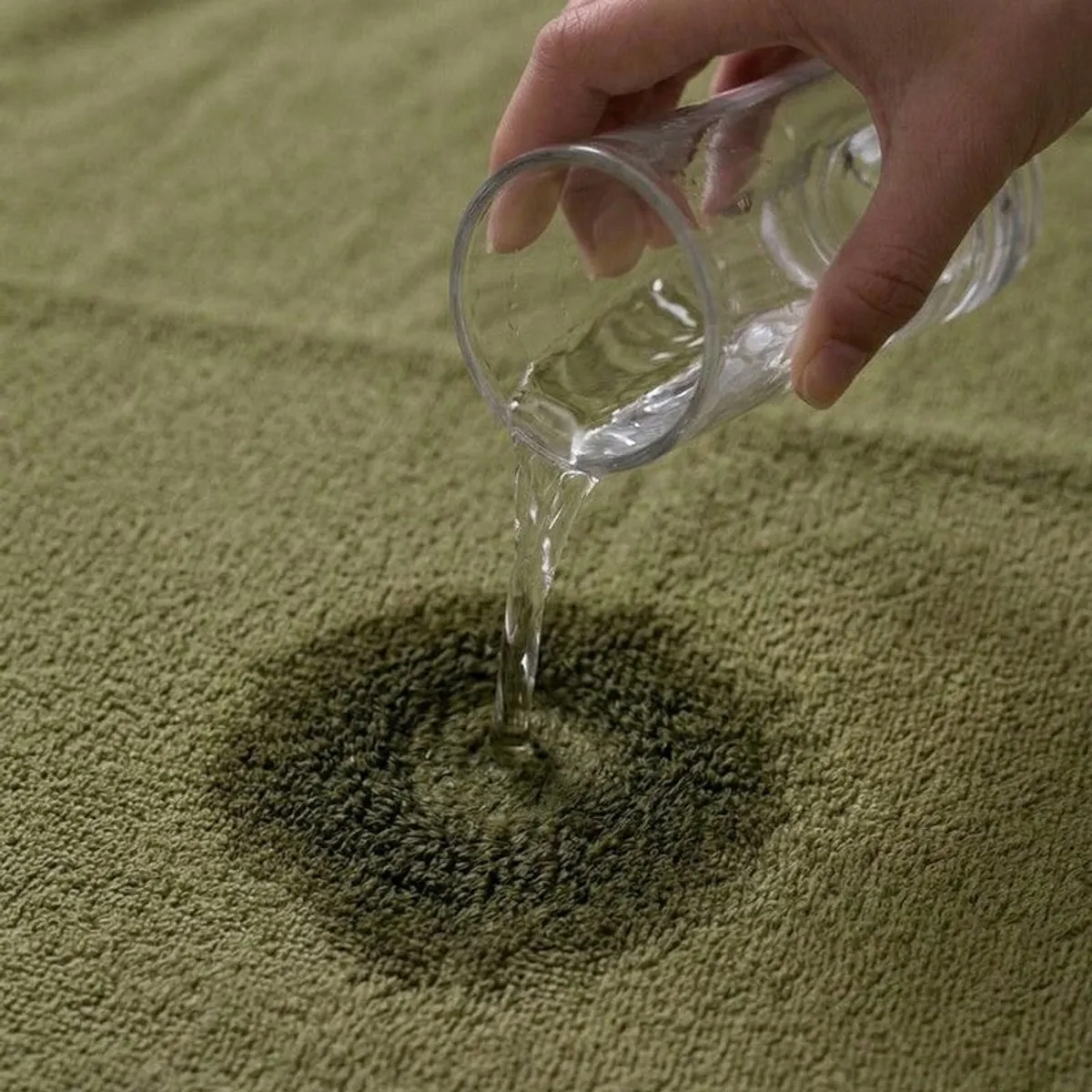 Water being poured onto the absorbent olive green towel surface