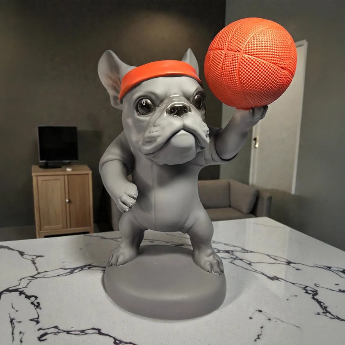 Front view of a grey bulldog figurine with orange headband and basketball