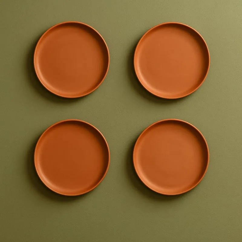 Four round terracotta wall plates arranged on an olive green wall