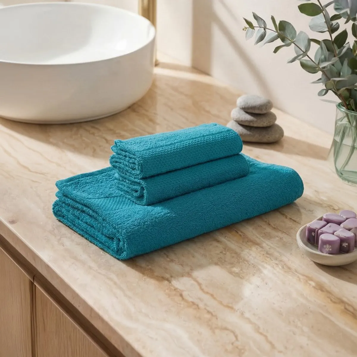 Folded blue towel set placed on a bathroom counter beside a basin