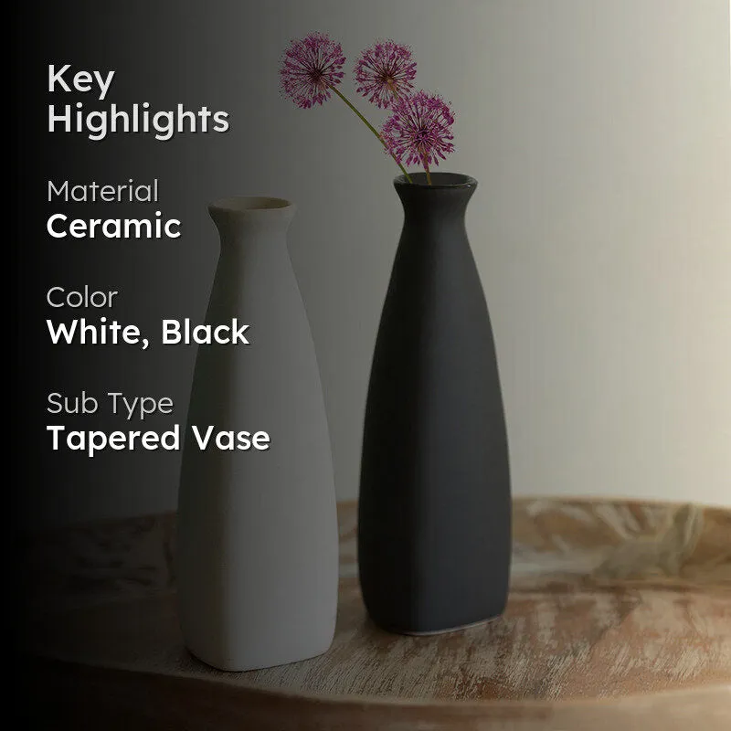 Black and white tapered vases on a wooden tray with pink flowers in the black vase