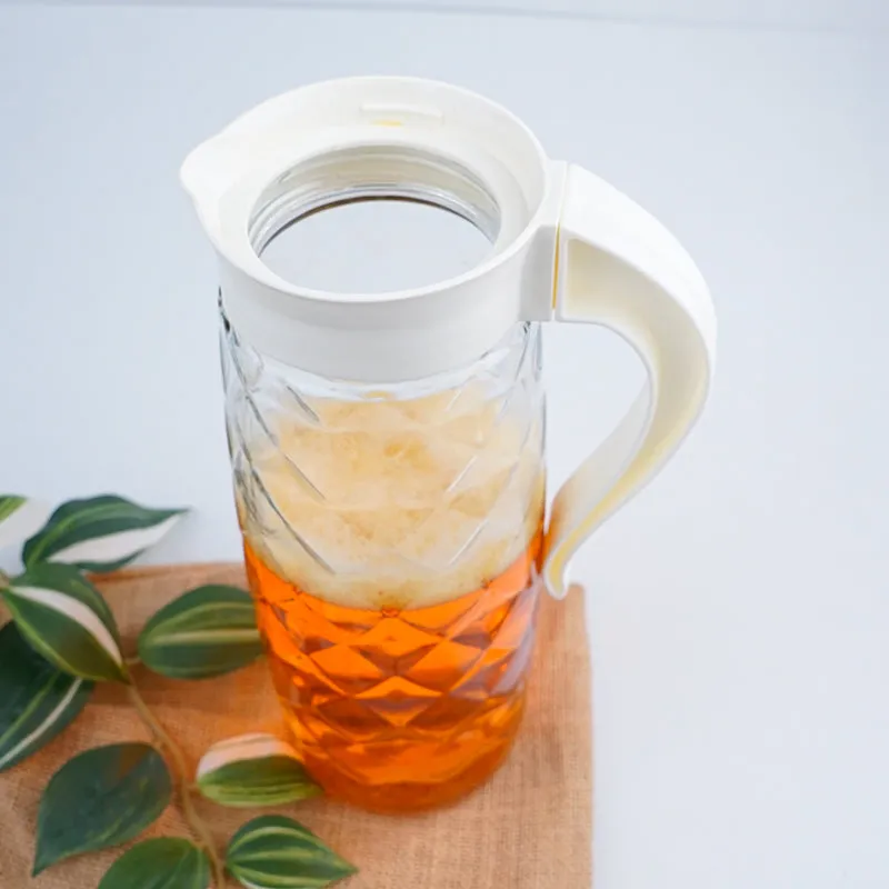 Transparent textured glass jug with white lid and handle, filled with amber drink