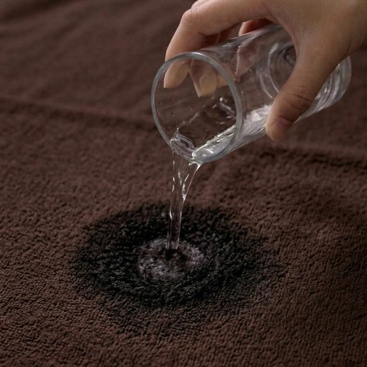 Water being poured onto the textured surface of a coffee brown bath towel.