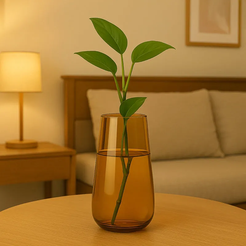 Brown glass vase with green stems on a wooden table beside a bed and lamp