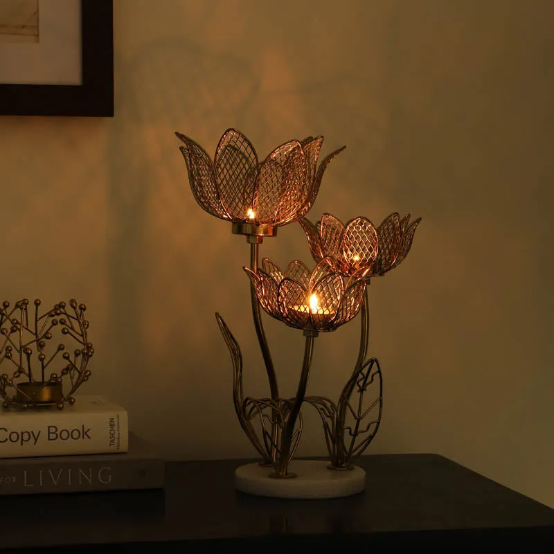 Lit lotus-inspired triple candle holder casting a warm glow on a tabletop