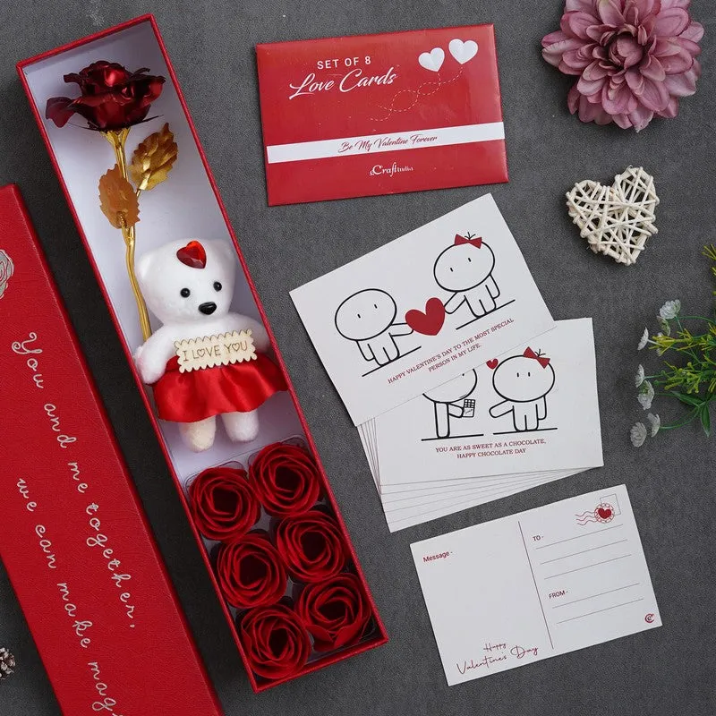 Open red gift box with teddy and rose beside a set of love cards