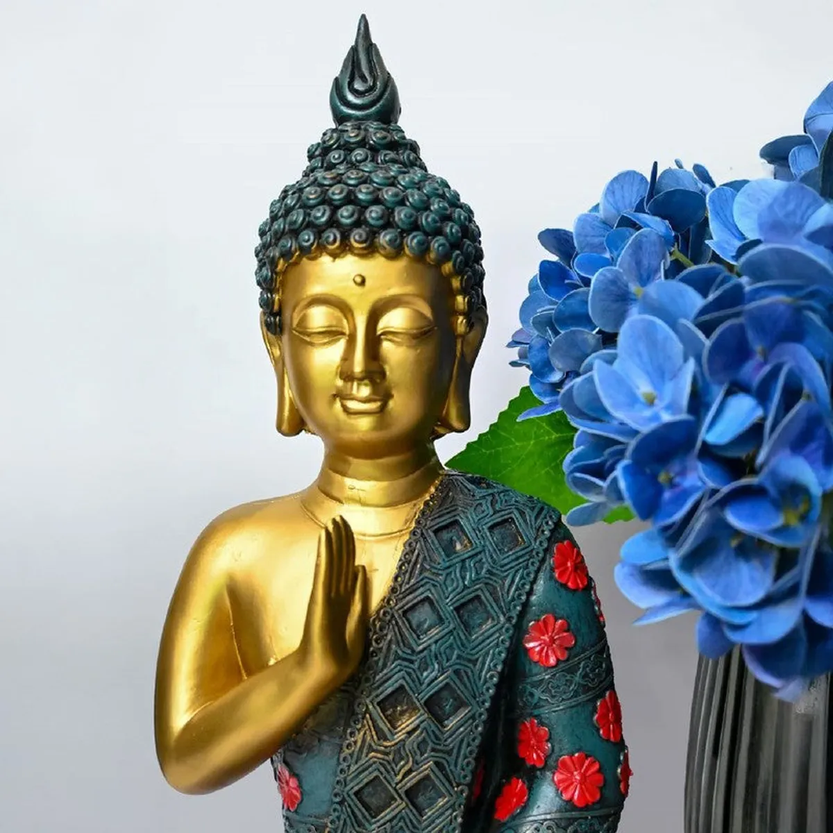 Close-up of Buddha idol with gold face, teal textured robe and red accents