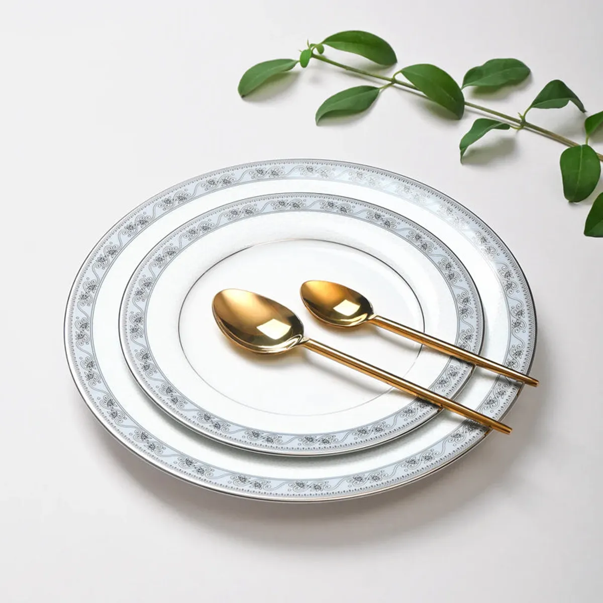 White porcelain plates with ornate borders arranged with gold-toned spoons.