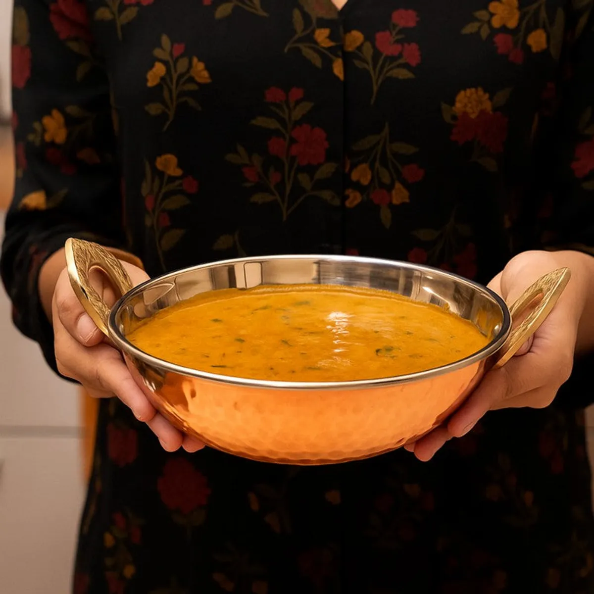 Copper kadhai filled with curry and held by its two side handles