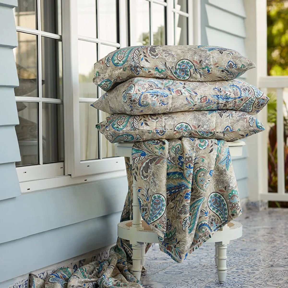 Folded floral paisley comforters stacked on a chair outdoors