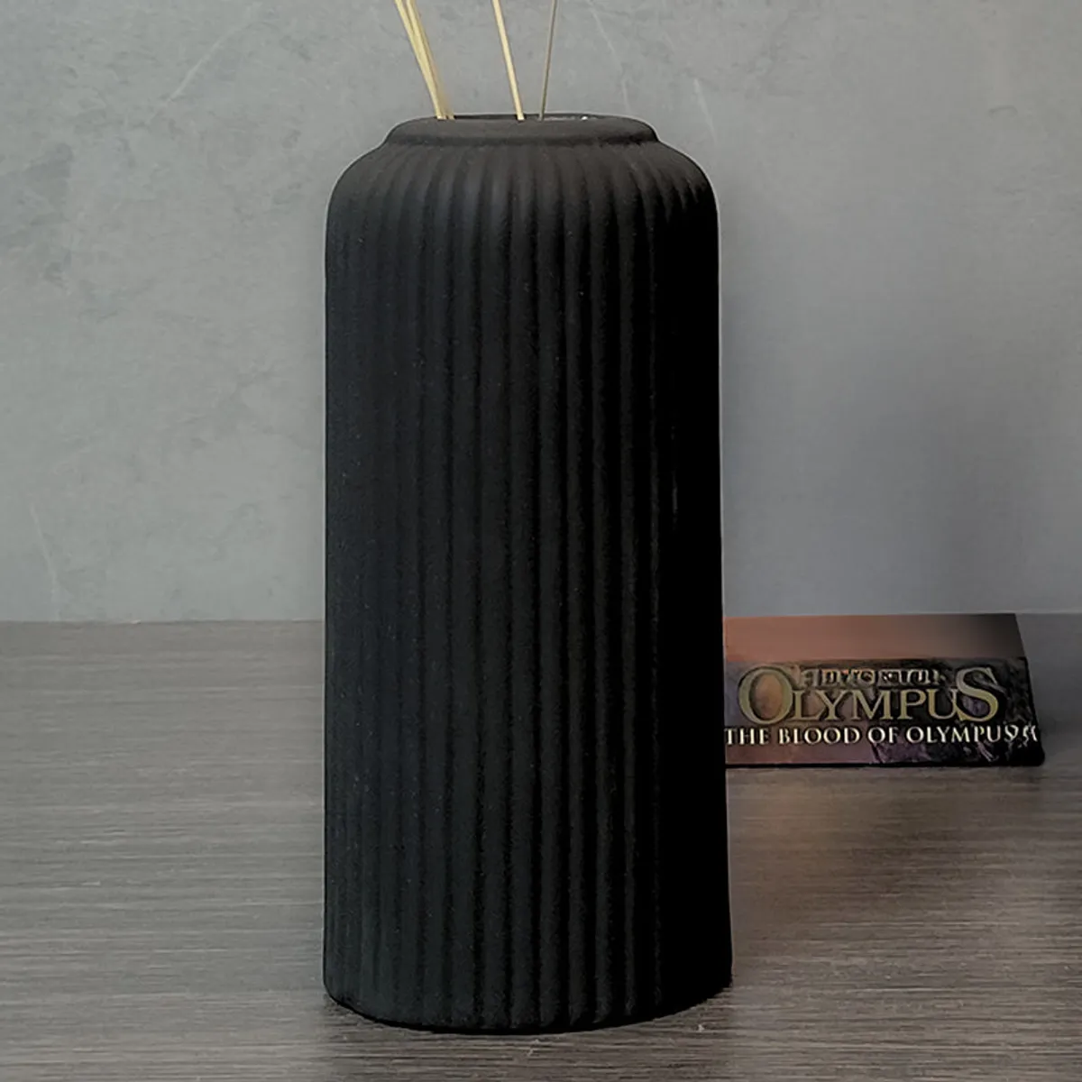 Black ribbed ceramic vase placed on a dark tabletop against a grey wall.