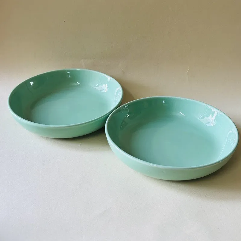 Two glossy green ceramic bowls displayed separately