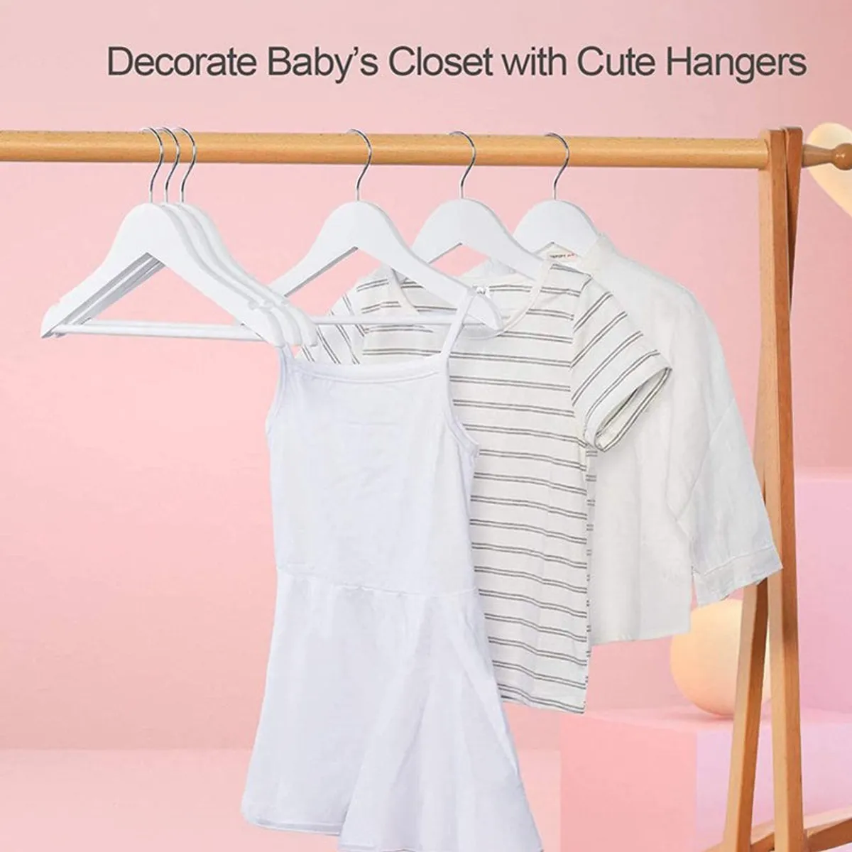 White hangers holding children’s clothes against a pink backdrop