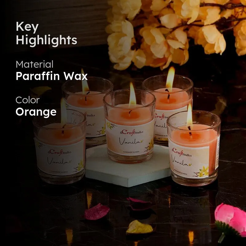 Five glowing orange votive candles arranged with flowers on a dark surface