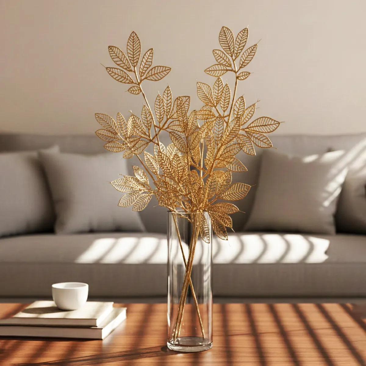 Golden artificial leaf stems styled in a vase on a white surface