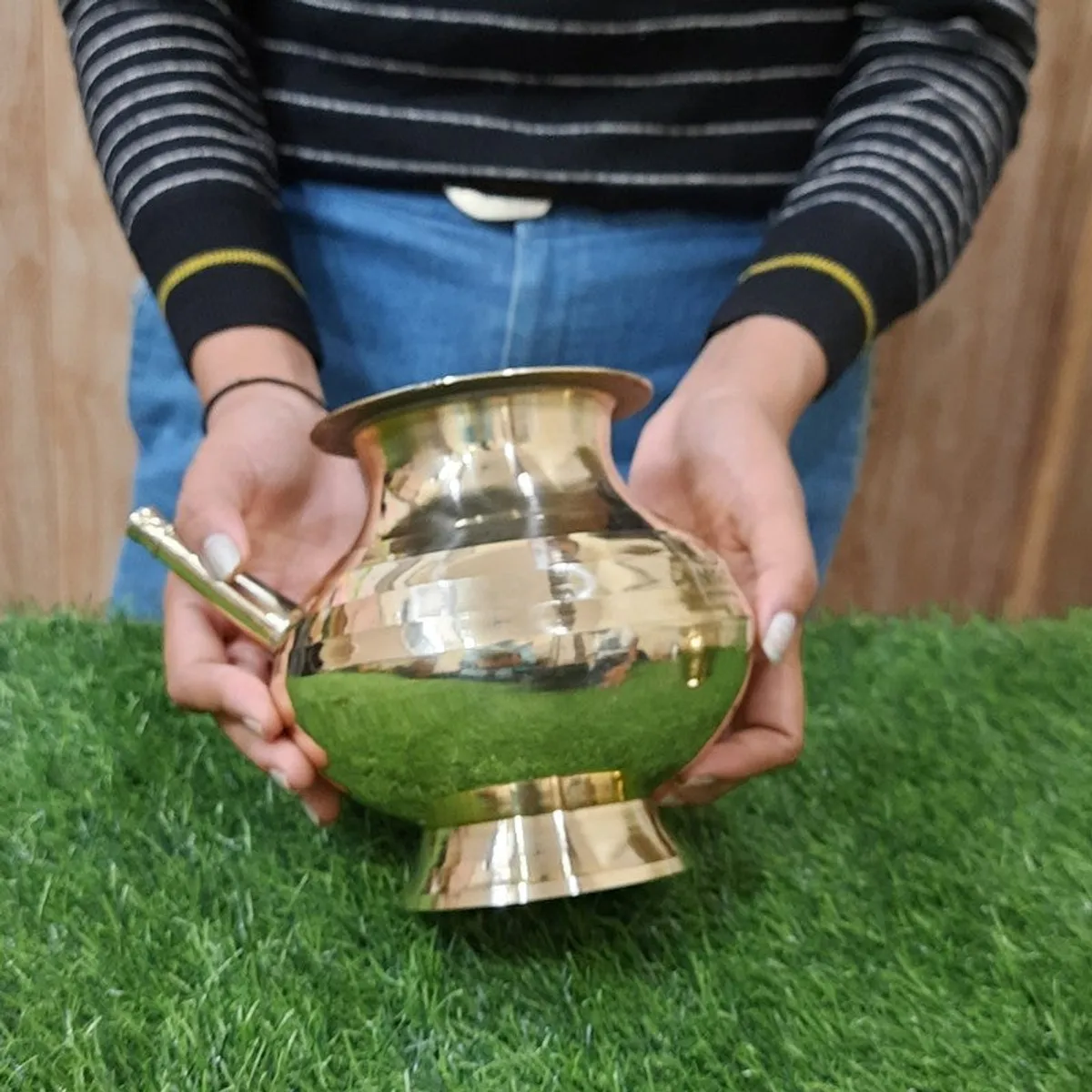 Person holding a polished brass kalasa with a side spout