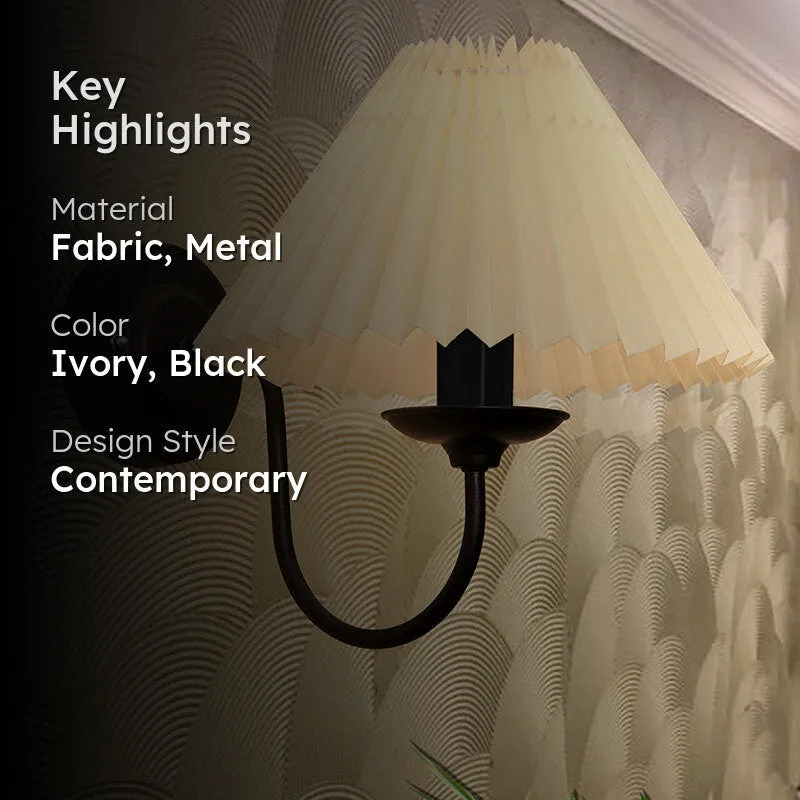 Lit wall lamp with ivory pleated shade and black metal arm against a textured wall