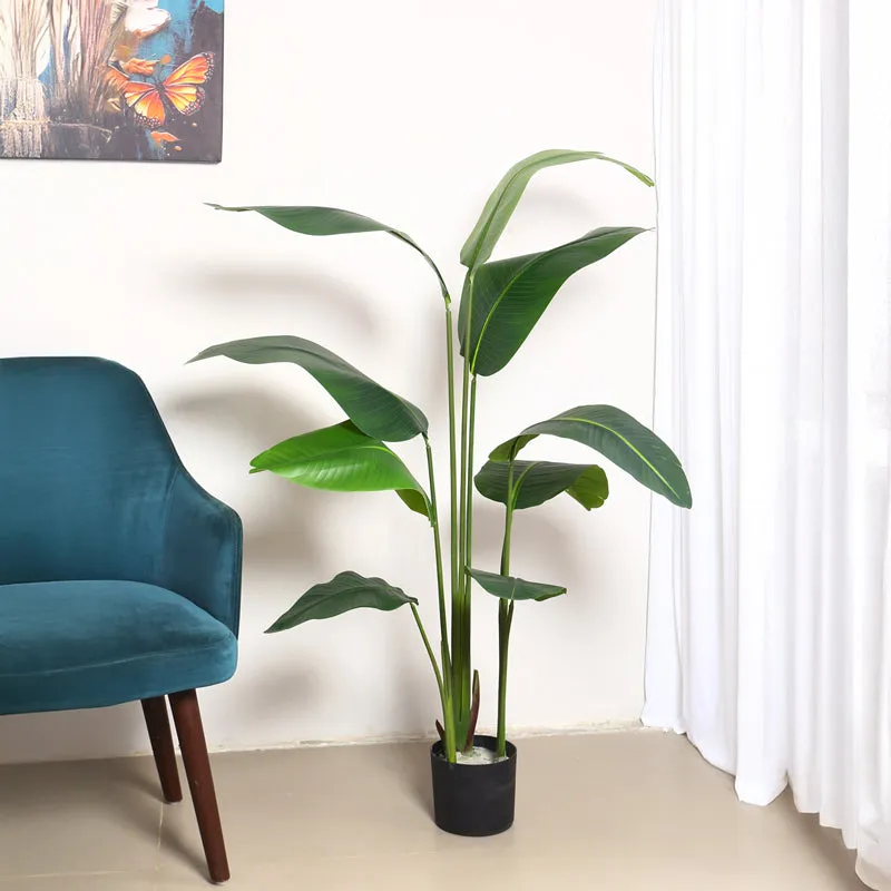 Tall artificial banana plant with broad green leaves in a black pot beside a blue chair