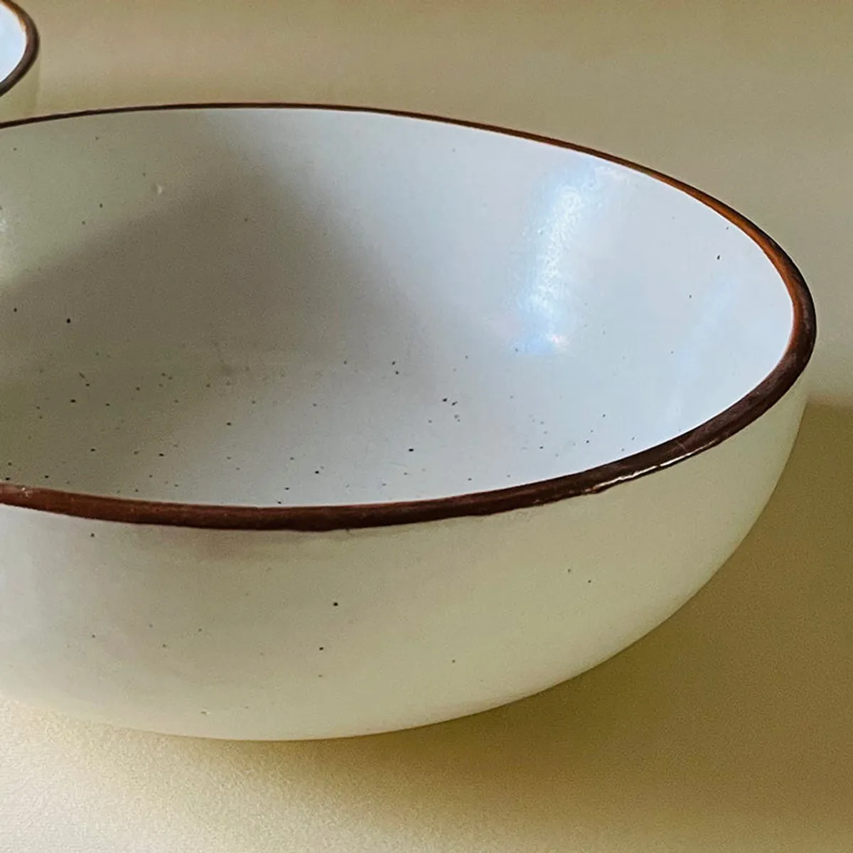 Close-up of a beige ceramic bowl showing its brown rim and glossy surface.