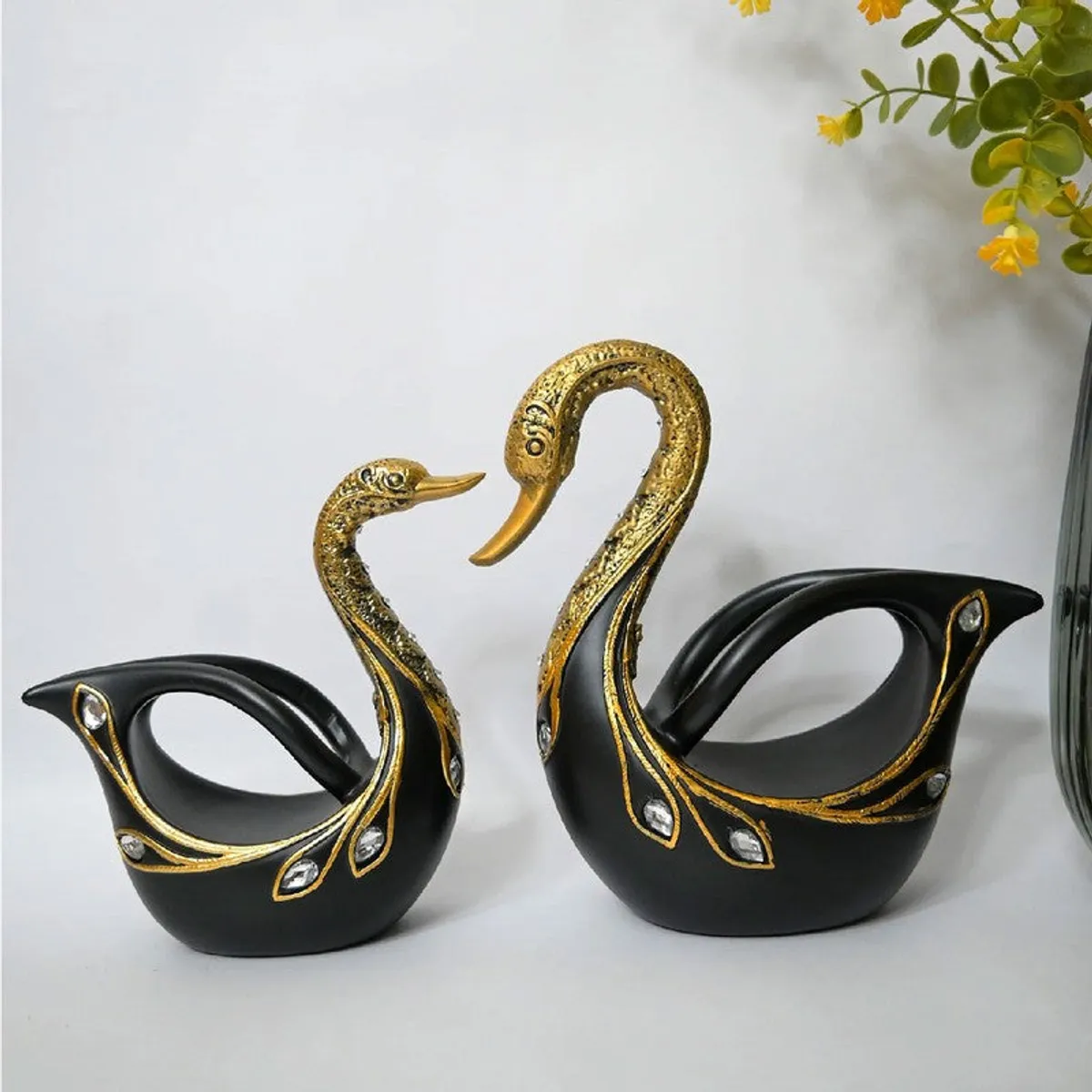 A large and a small black and gold swan showpiece styled together on a white surface.
