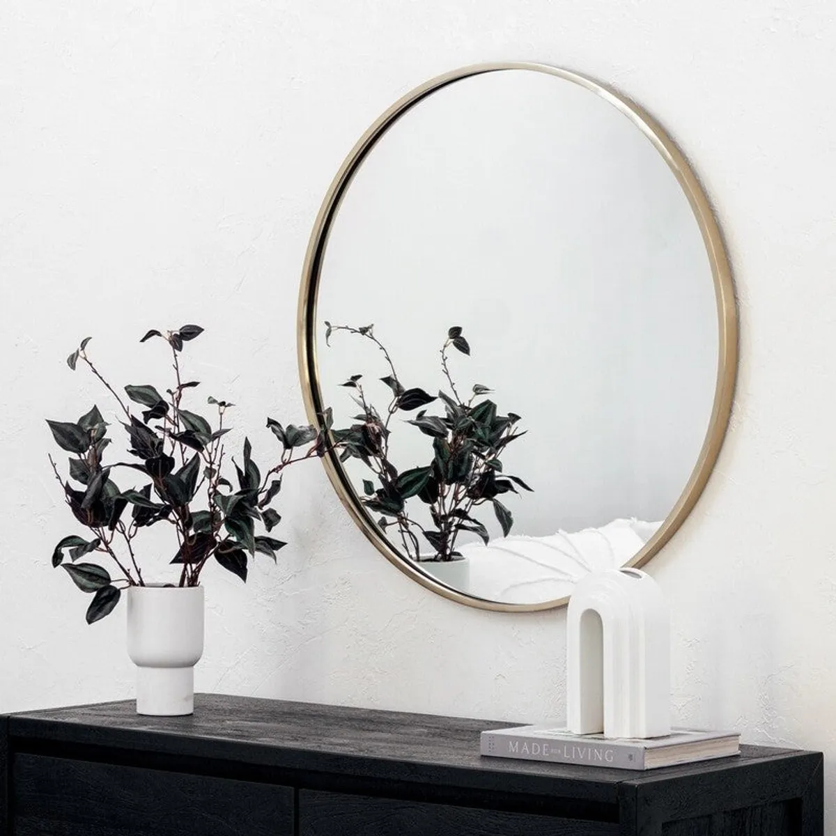Round gold-framed wall mirror reflecting plants and a contemporary room