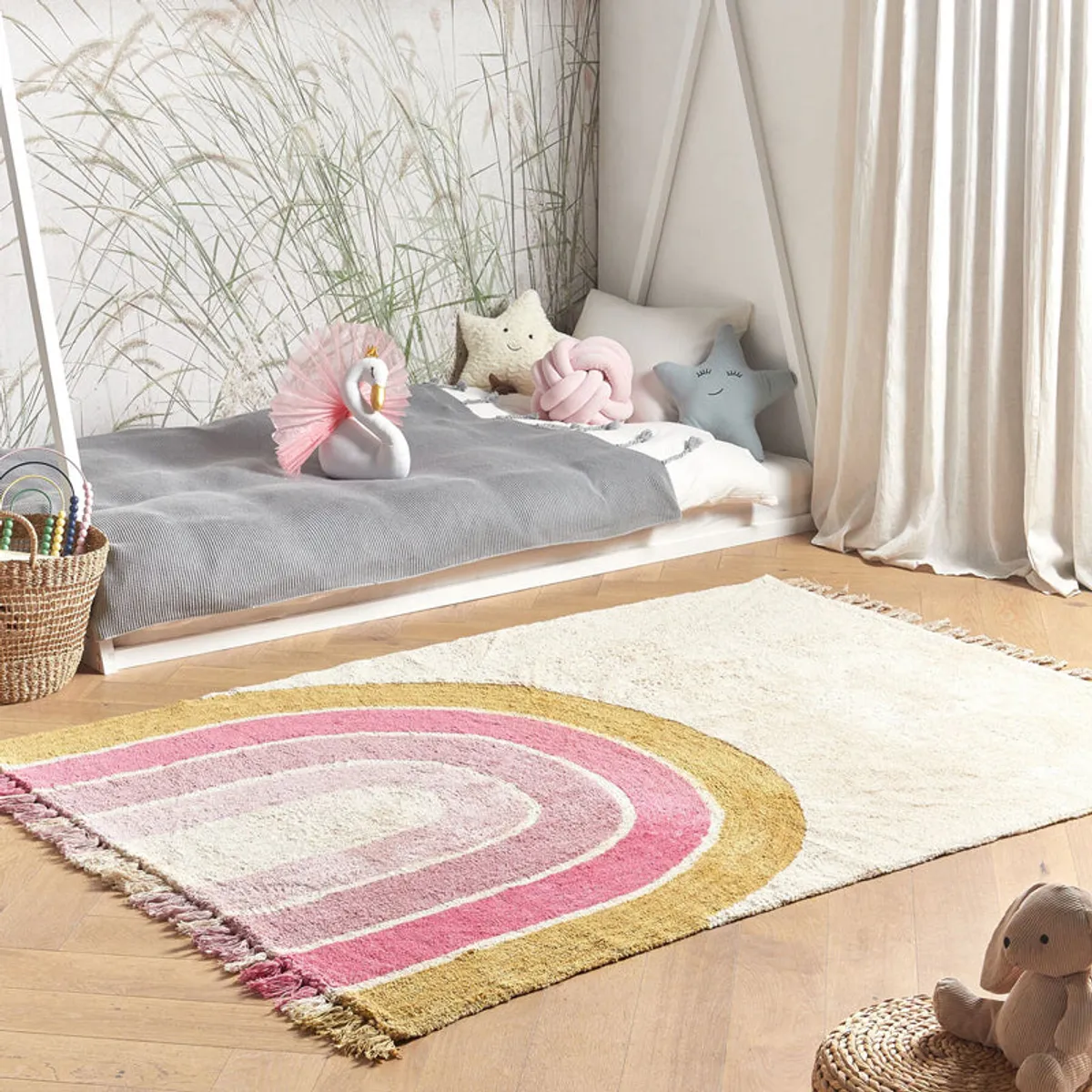 Rectangular rainbow arc cotton rug in pink, cream and gold styled in a children's room