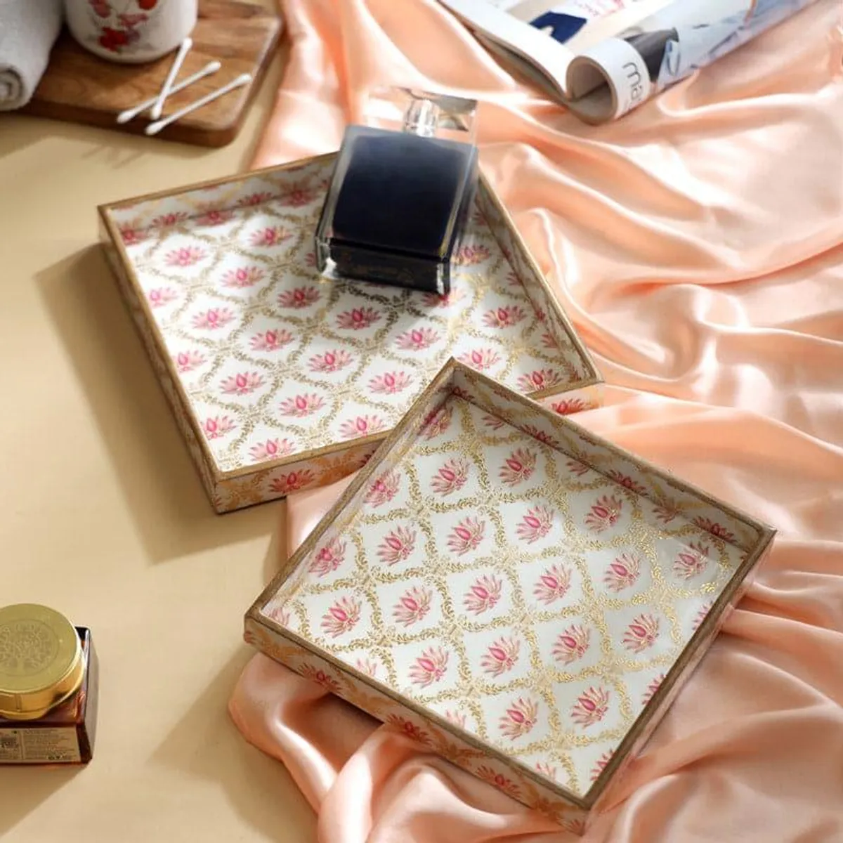 Two square floral trays styled on peach fabric with decorative objects
