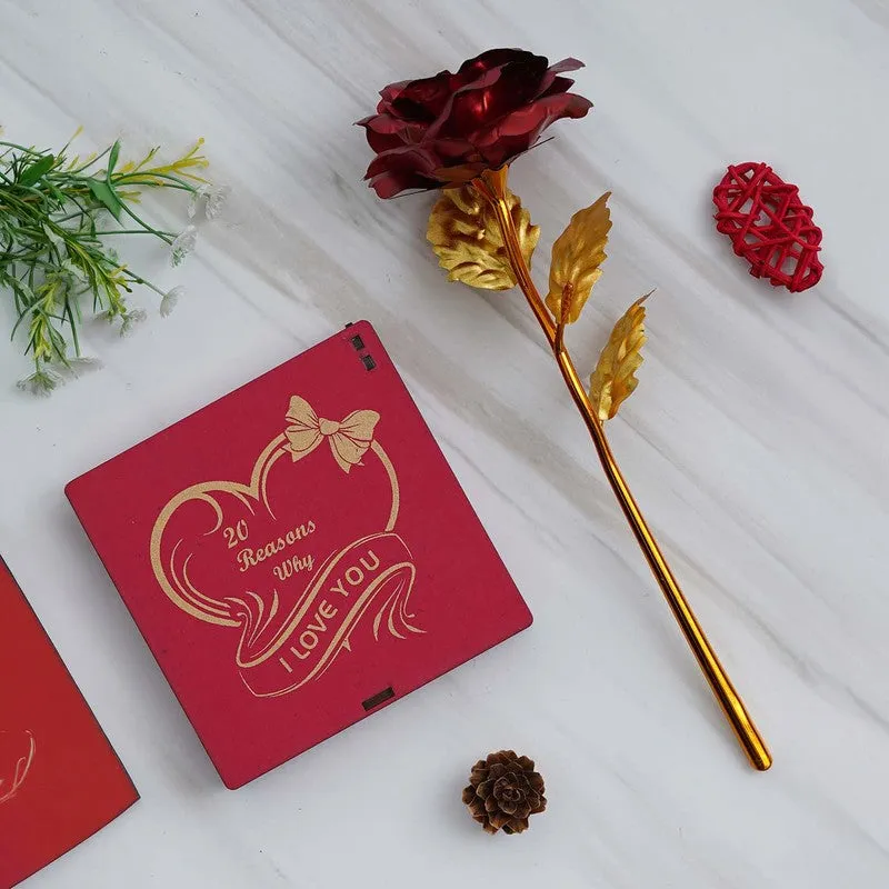 Closed red gift box with gold heart motif beside a metallic red rose