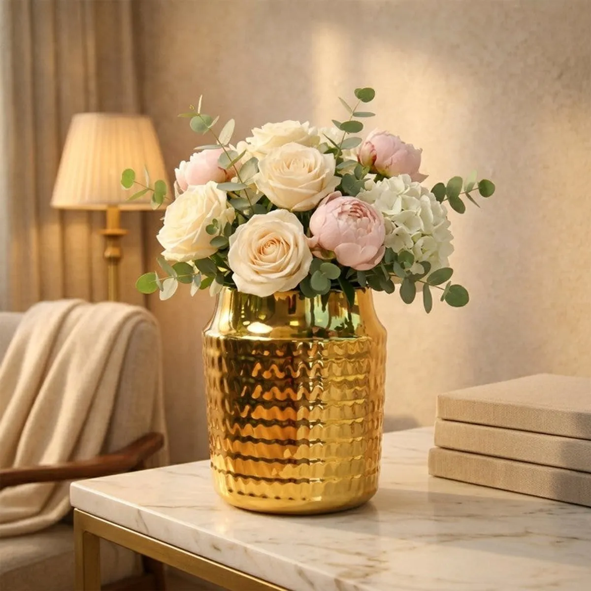 Gold ribbed ceramic vase with cream and blush flowers on a marble tabletop.