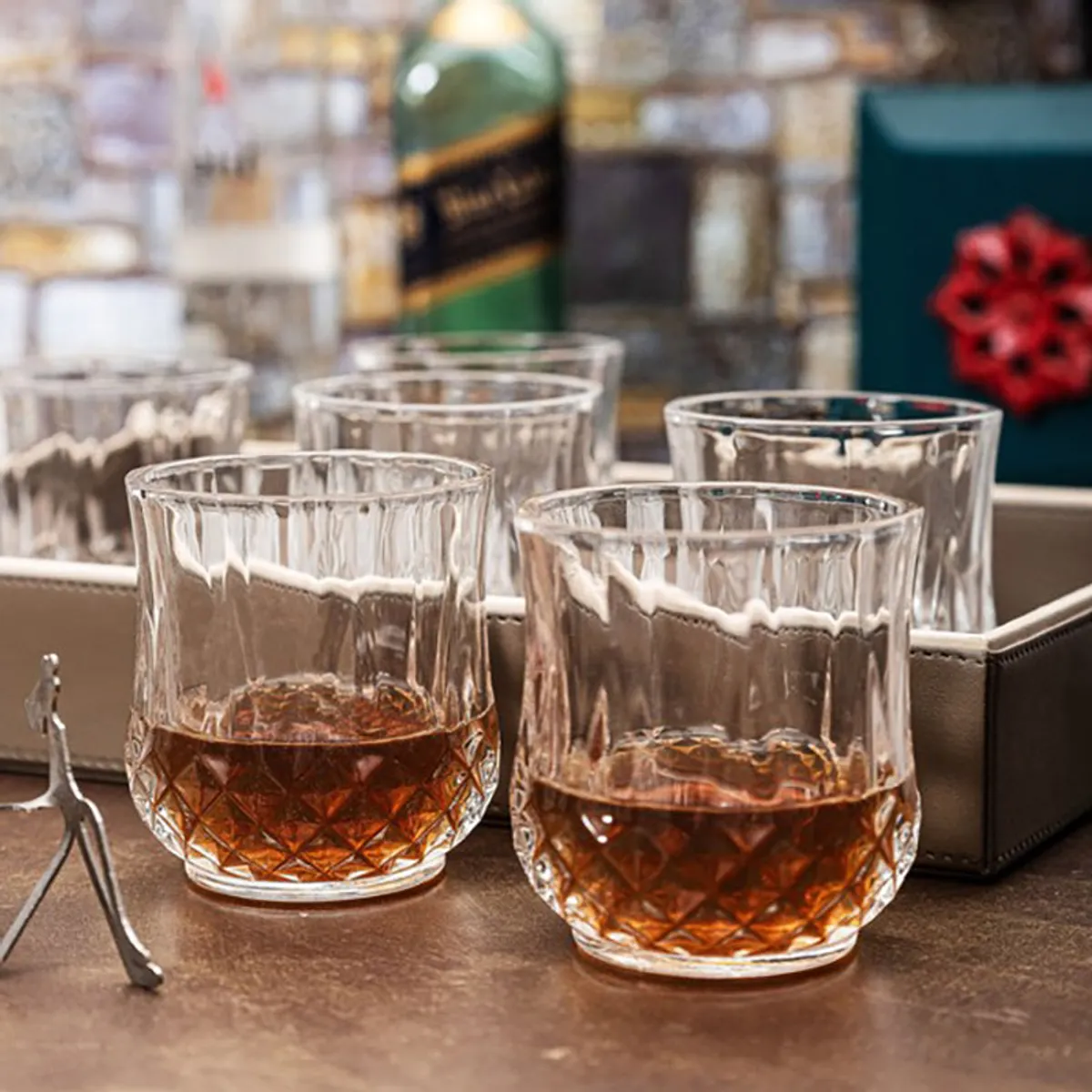 Clear patterned whiskey glasses filled with amber whiskey on a bar setting
