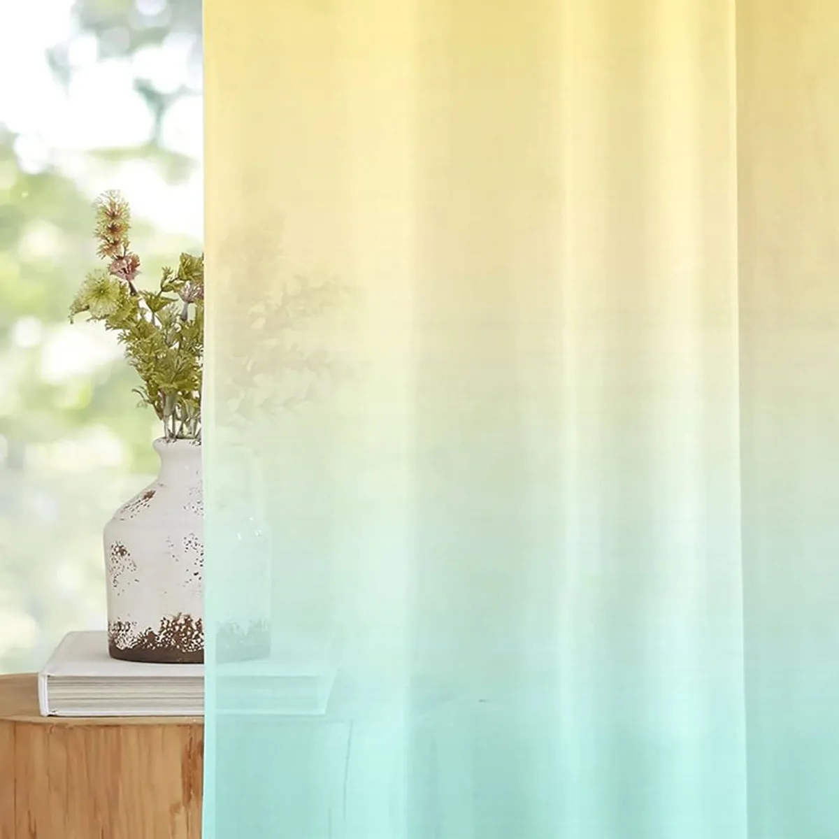 Sheer ombre curtain filtering light beside a vase and window