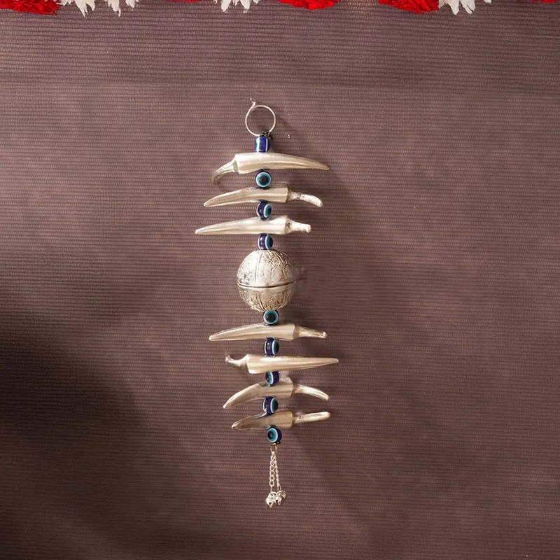 Single silver nimbu mirchi latkan with blue beads hanging against a brown wall