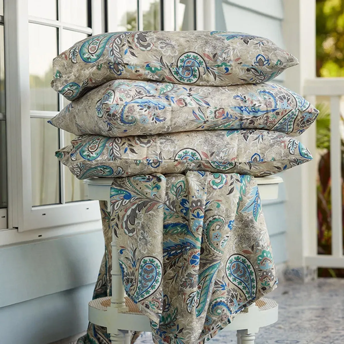 Folded blue and beige paisley bedding displayed by a window
