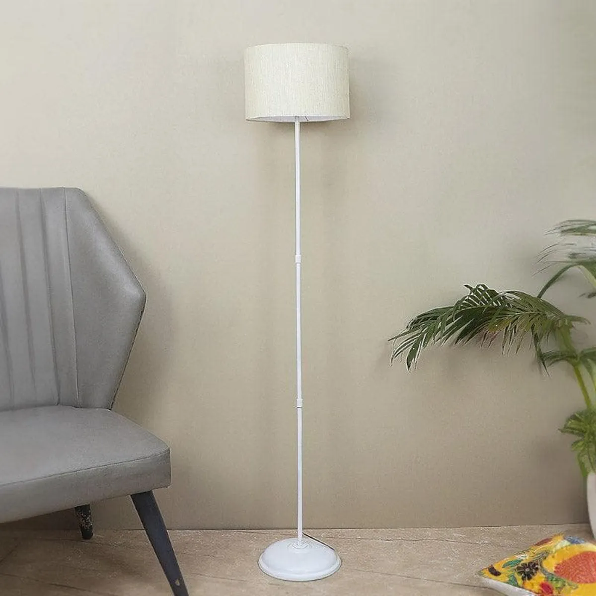 White floor lamp with beige fabric shade beside a grey chair and indoor plant