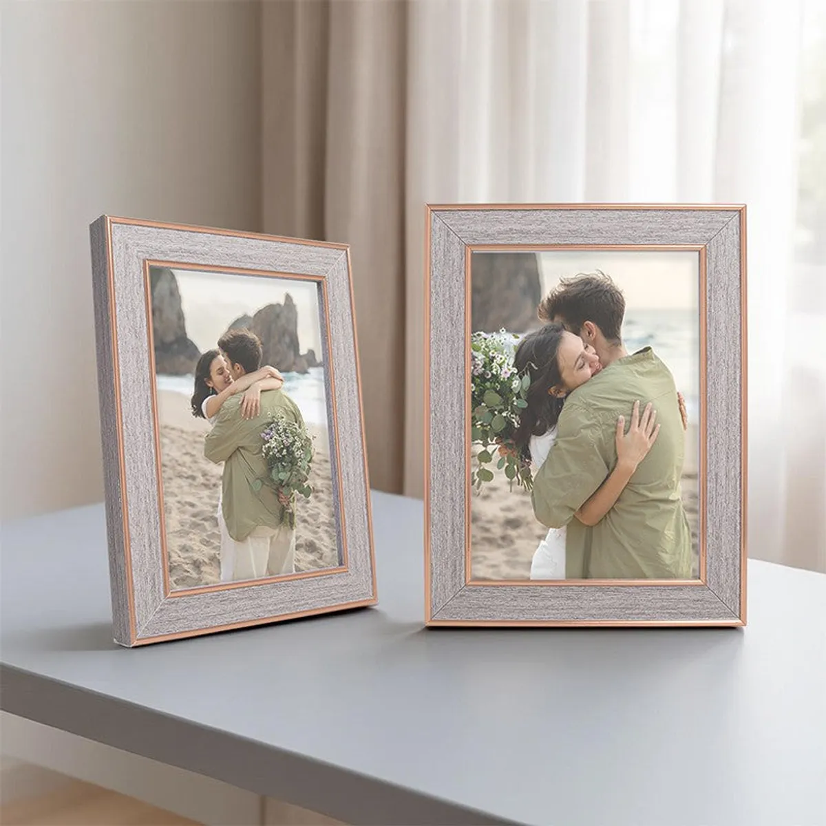 Two rectangular grey and gold photo frames on a tabletop by a bright window
