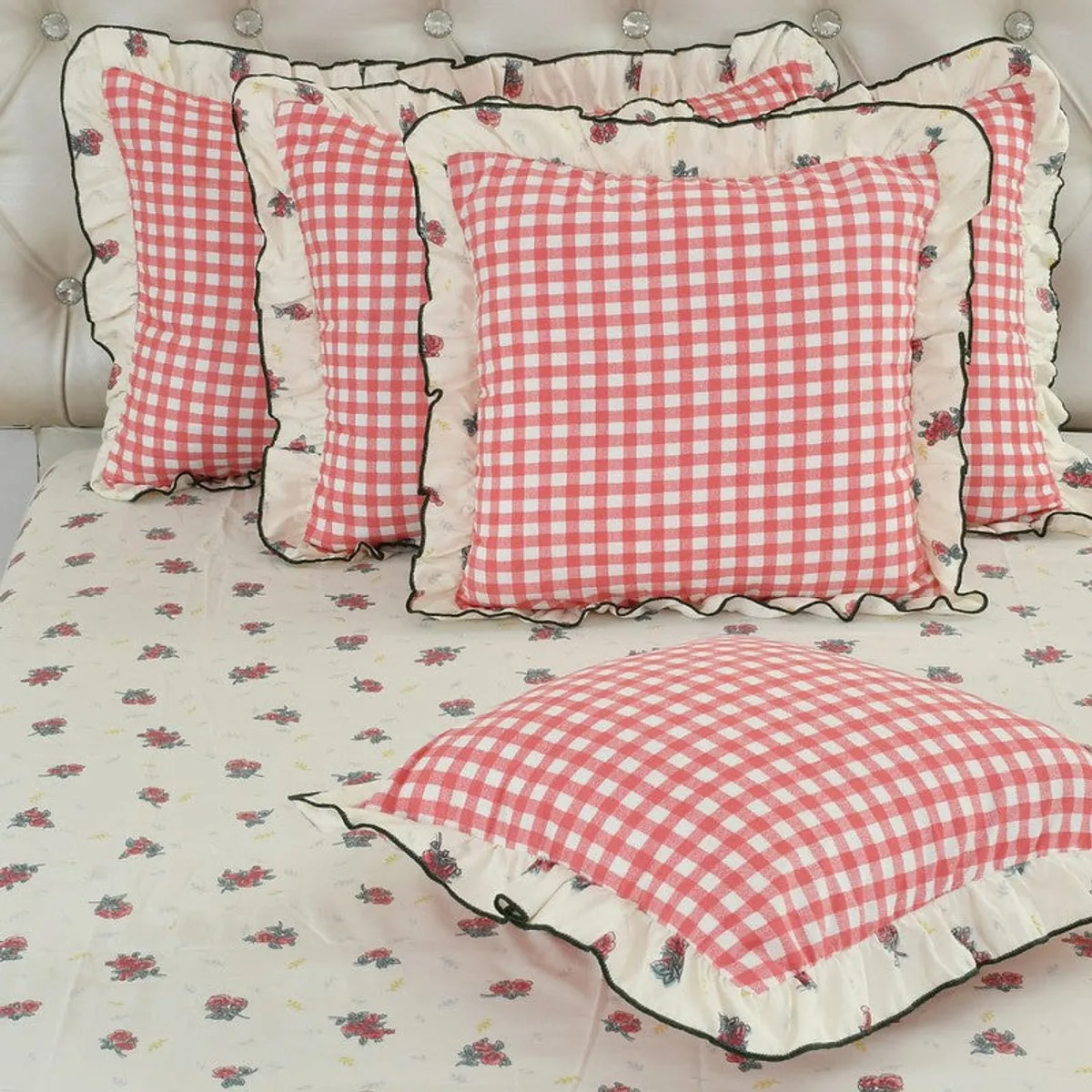 Close-up of pink checked cushion covers with ruffled floral borders on floral bedding