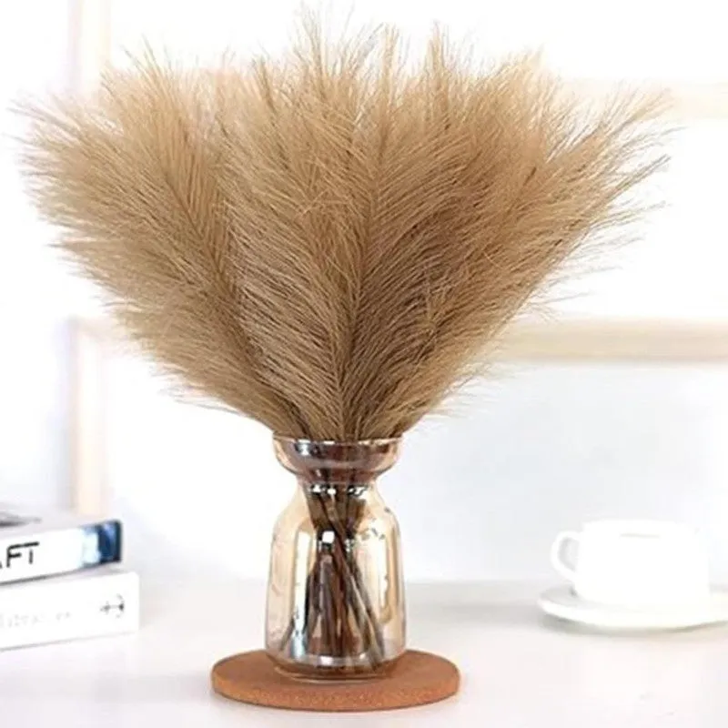 Brown feathery pampas stems arranged in a reflective vase on a tabletop