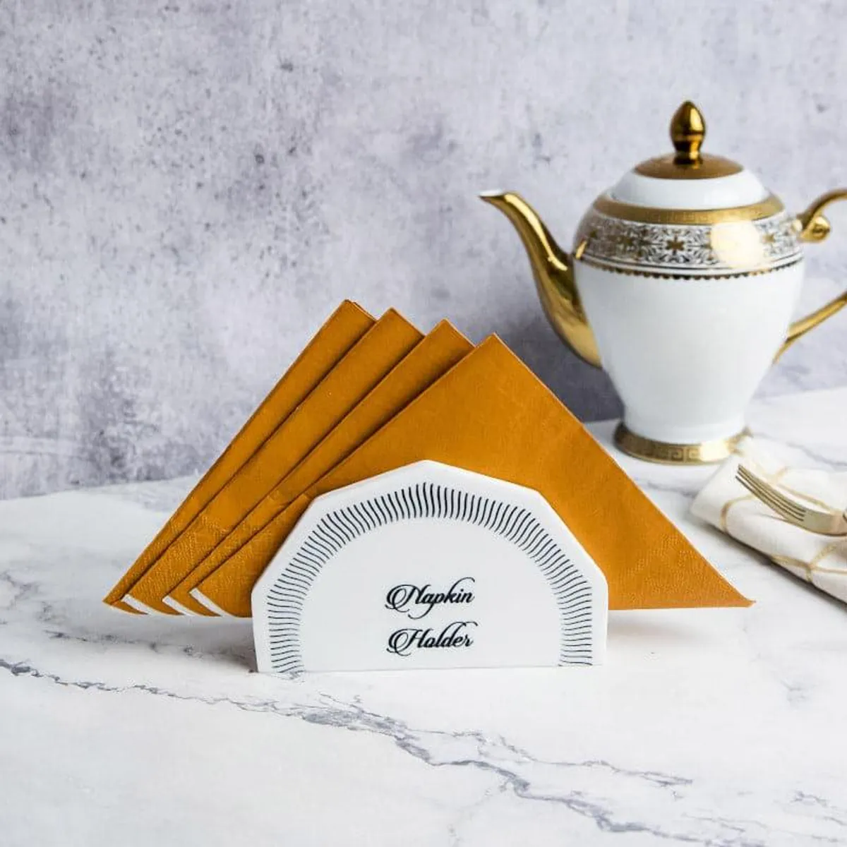 White marble napkin holder displaying folded mustard napkins on a table.