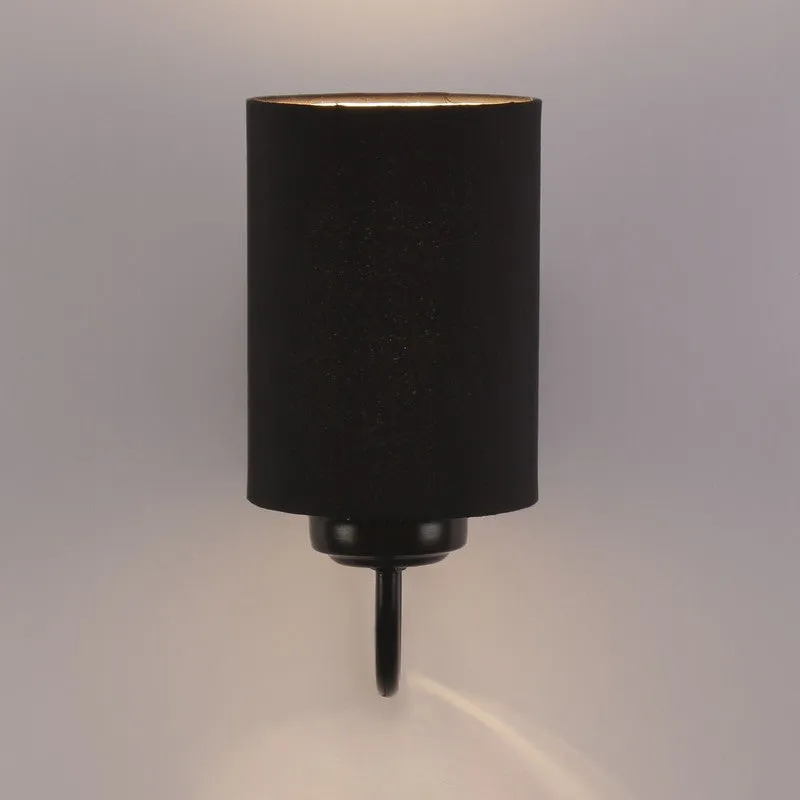 Black cylindrical wall lamp glowing against a light wall