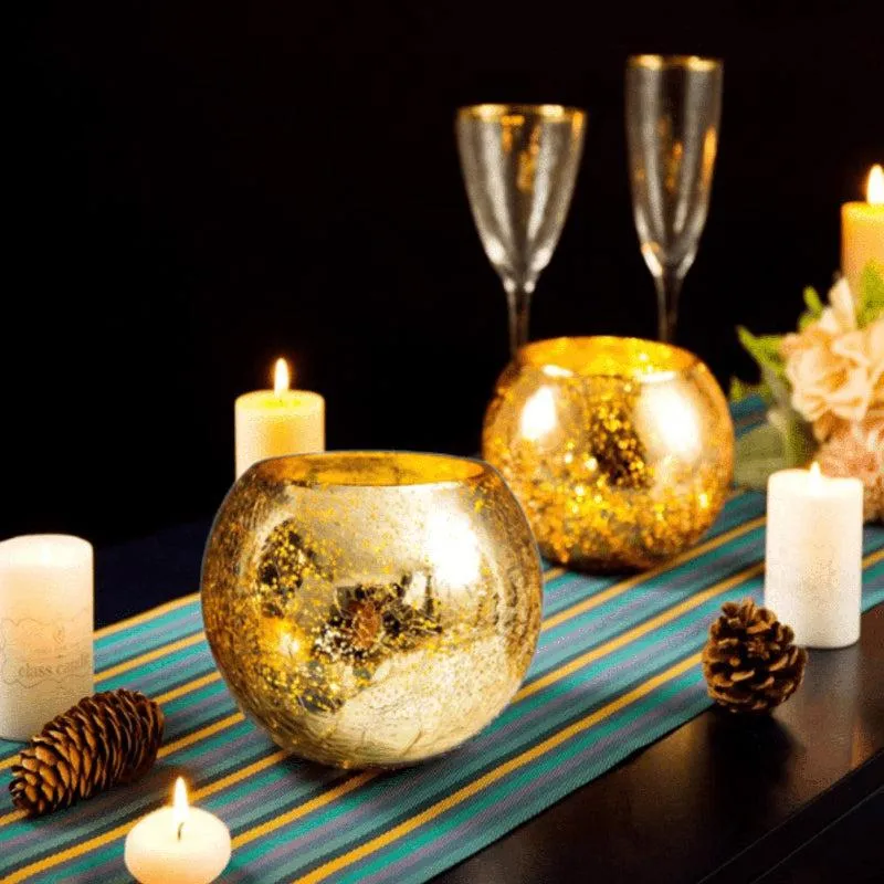 Gold glass candle holders glowing among candles, flowers and glassware on a table